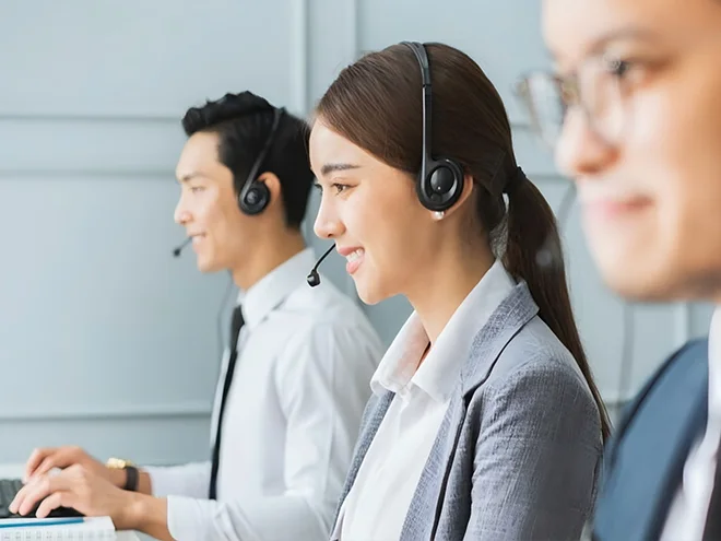 Three people are wearing headsets and smiling at a computer.