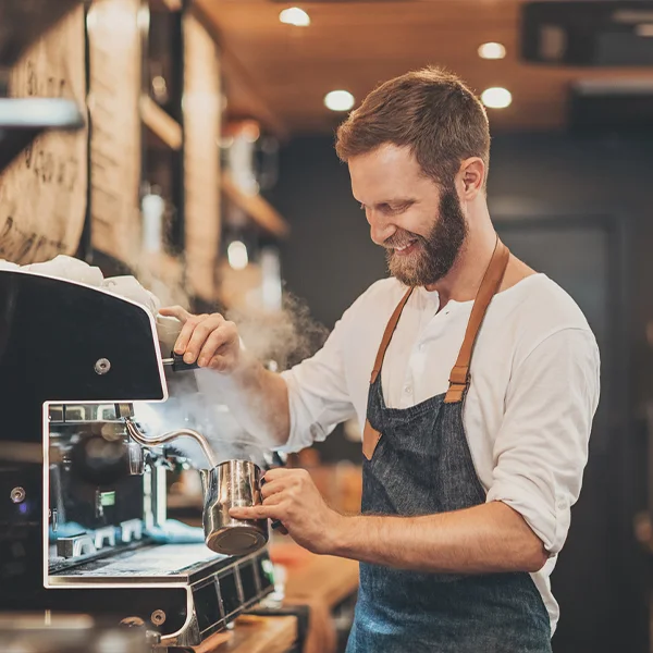 A barista is making coffee in front of a machine.