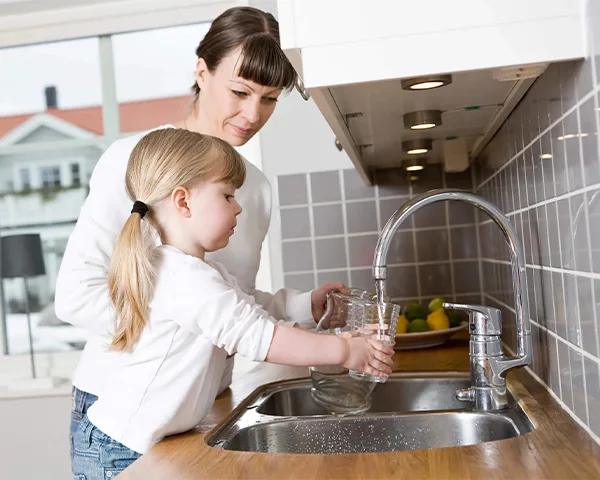 A little girl filling a cup with water accompanied by her mother