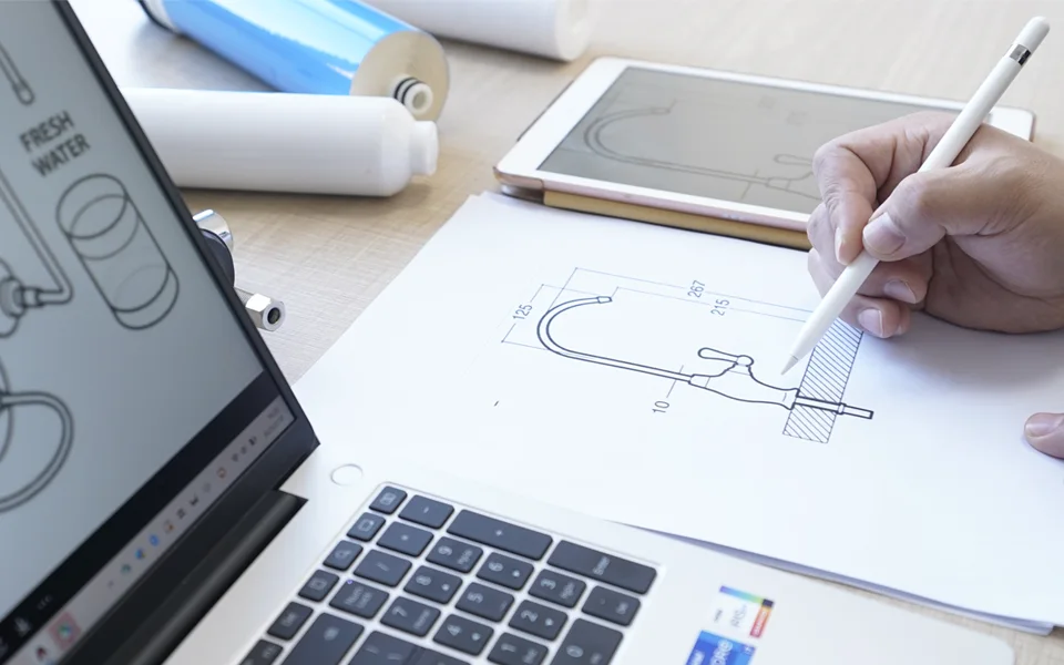A person is drafting a faucet design drawing at a desk.