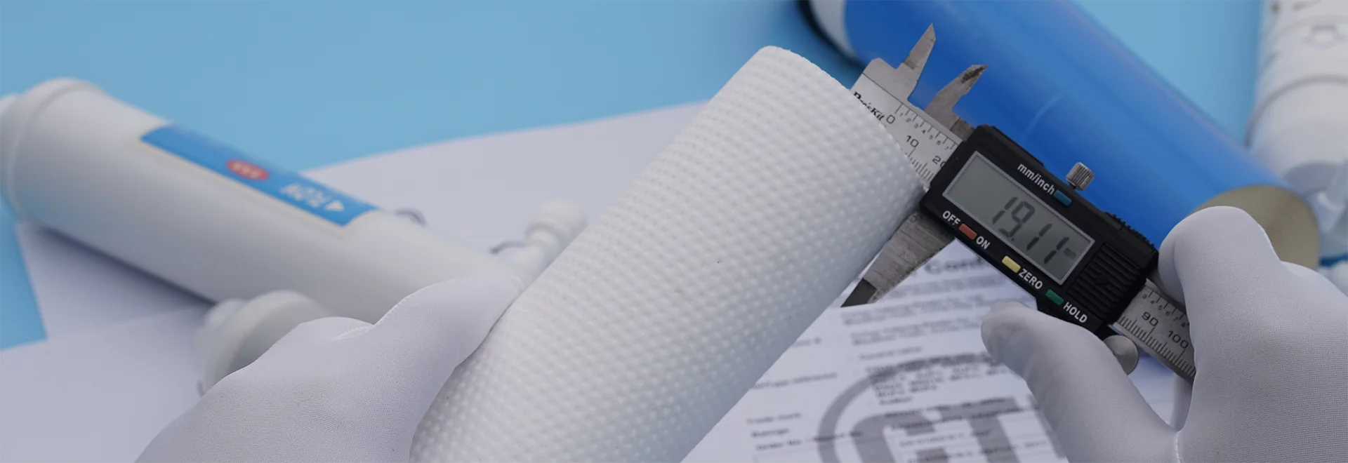 A person is measuring the thickness of a filter cartridge on the desk.