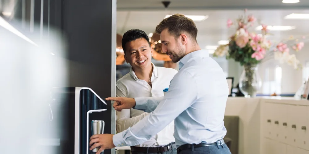 2 men are talking in front of a water dispenser.