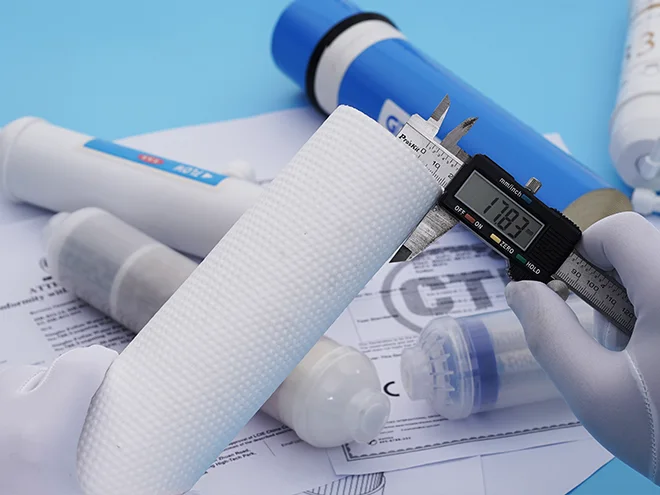 A worker is measuring the specifications of a filter cartridge on the table.