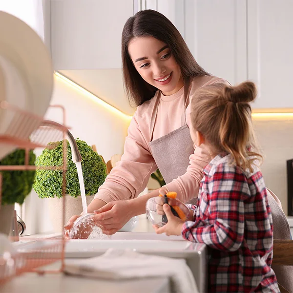 A woman smiling at a girl while washing dishes