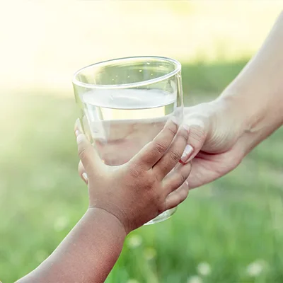 An adult is giving a kind a glass of water.