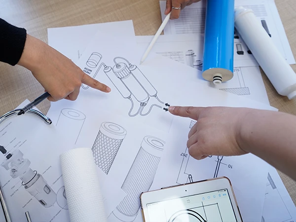 Varias personas están señalando los cartuchos de filtro y los dibujos sobre la mesa.